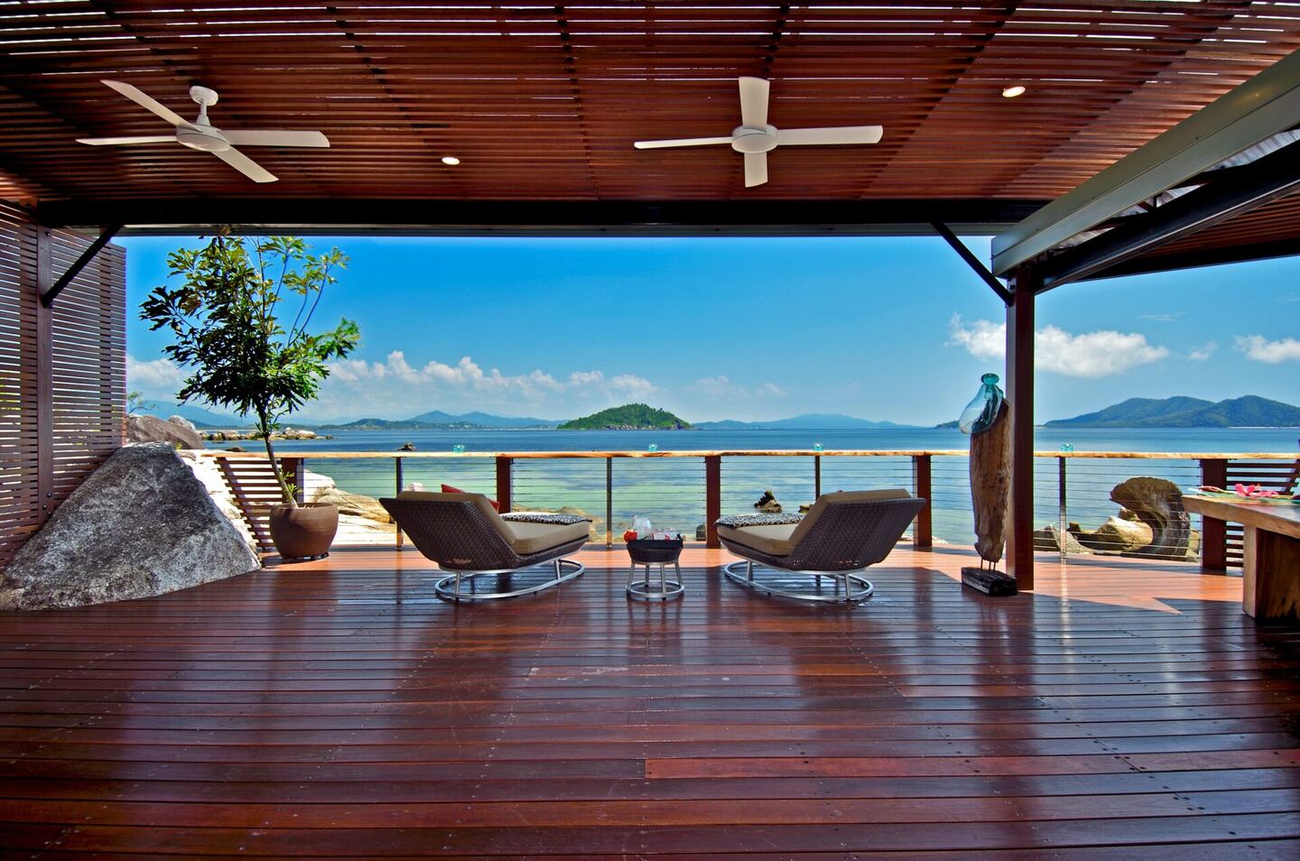 Covered timber deck with sun lounges and ceiling fans looking over the Coral Sea