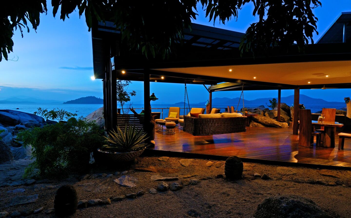 The retreat's deck and living area lit up at dusk above the rocky shoreline