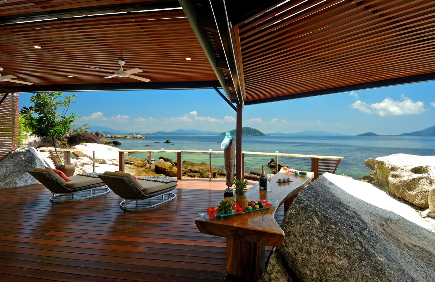 Sun lounges on the covered deck with tropical fruit on a side table and islands beyond