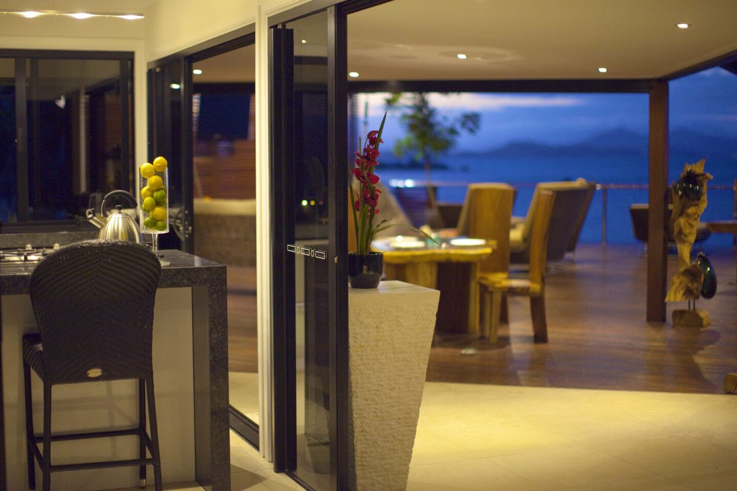 Indoor dining and lounge area lit warmly at night above the sea