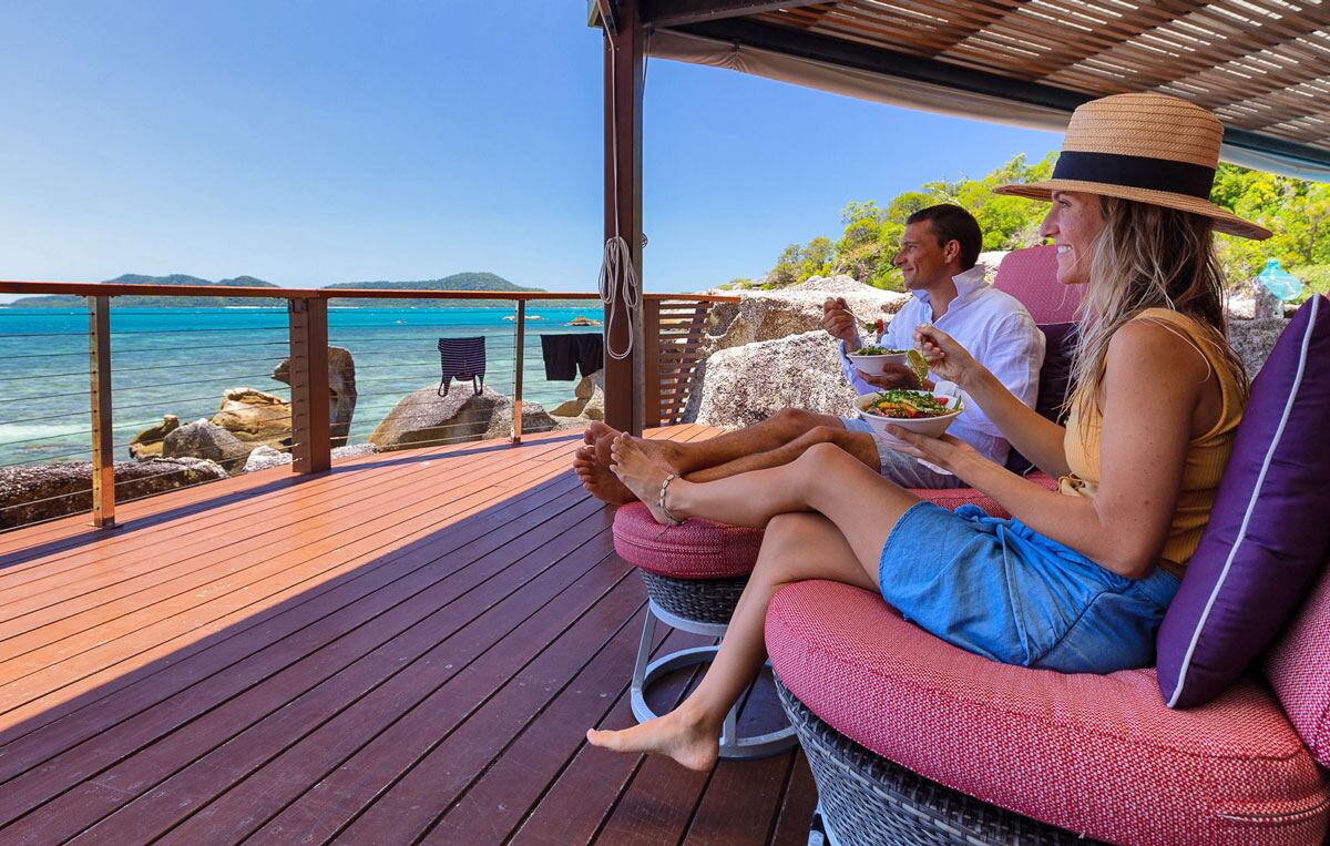 Two guests relaxing with drinks on a daybed on the deck