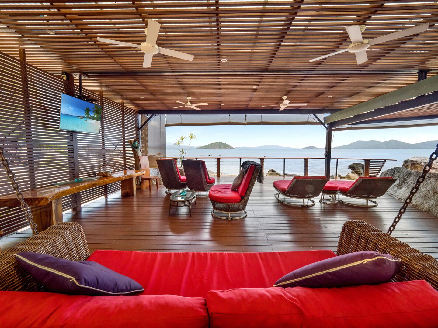 Covered deck with a red daybed and sun lounges facing the sea
